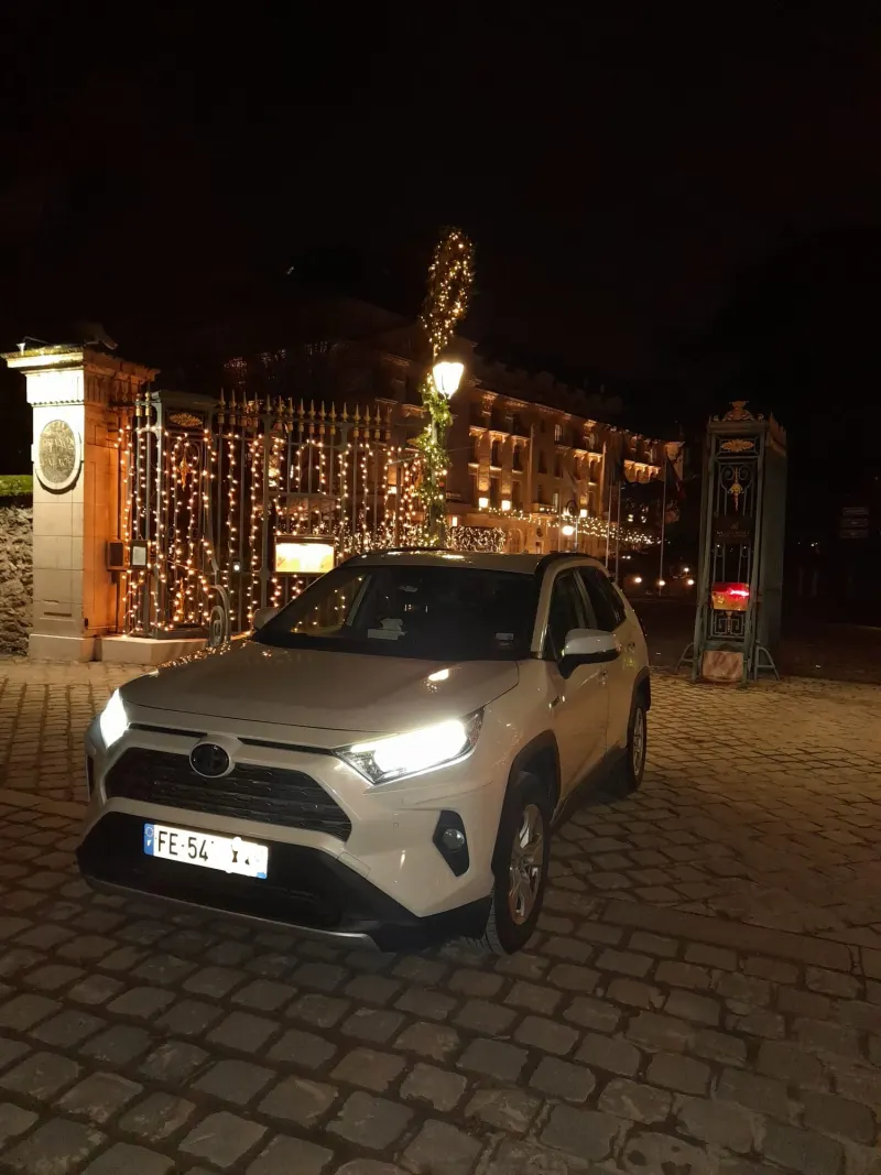 Le SUV blanc de Kams Transports, de nuit, devant un hôtel illuminé